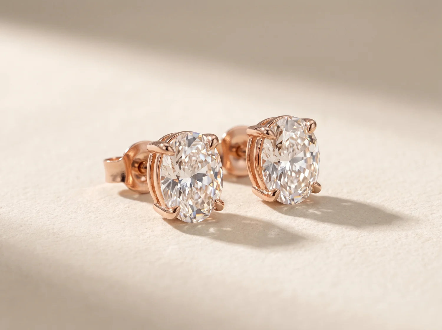 Oval diamond stud earrings in rose gold on an ivory surface